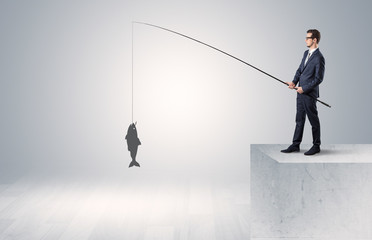 Young businessman fishing golden fish from the top of a building
