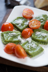 Close-up of spinach ravioli with cherry tomatoes and grated parmesan, selective focus