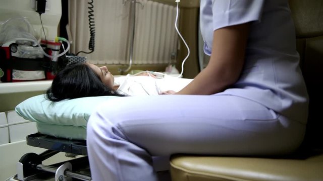 Accident victim inside ambulance at night being treated by nurse. Chinese young female patient laying in bed in ambulance with beautiful female nurse checking her conditions. Sliding dolly shot.