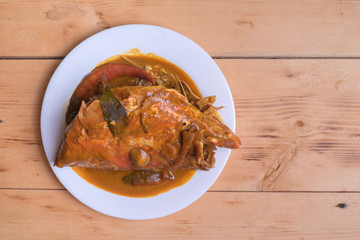 Malaysian red fish head curry in white plate over the pine wood