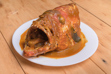 Malaysian red fish head curry in white plate over the pine wood