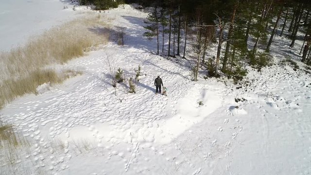 Man and a boy on a island, C4k aerial view around a uncle and a kid walking at a lake, in Teijo national park, on a sunny winter day, Varsinais-suomi, Finland
