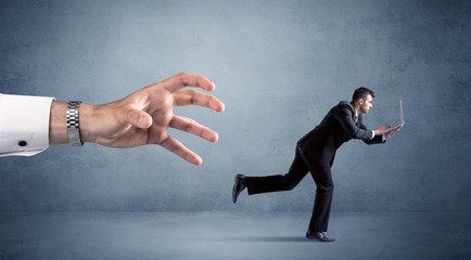 Young miniature businessman running from a big hand 