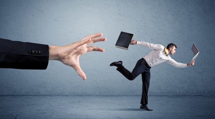 Young miniature businessman running from a big hand with blue background