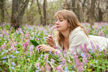 A pensive dreamy woman looks at a bouquet of flowers in her hands lying in a meadow with flowering forest grass