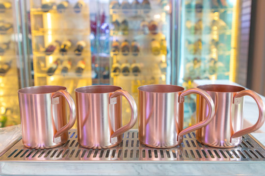 Cup Stainless Steel of copper or pink gold Put on a stainless steel tray. The back is a wine bar and wine cooler with golden light blurred the background.