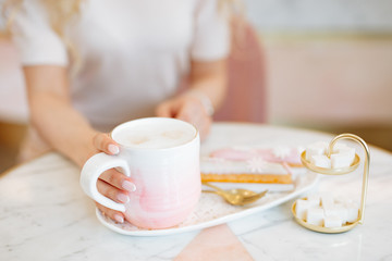 Delicious handmade eclairs with pink glaze and a Cup of coffee on the table in the cafe. Pink background.