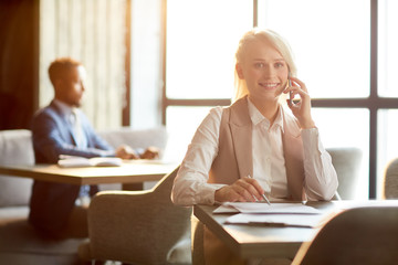 Young manager or agent looking at camera while sitting by table in cafe and consulting clients by smartphone