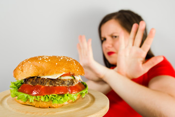 Young fat girl crossed arms closing from burger on gray background
