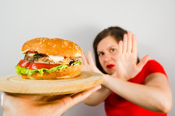 Young fat girl crossed arms closing from burger on gray background