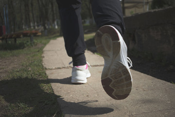Fototapeta na wymiar girl's legs in sneakers run on a concrete road, morning exercises, sports concept