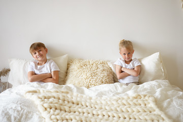 Cute blonde little boy relaxing in bedroom, sitting in bed together with his elderly brother, both...