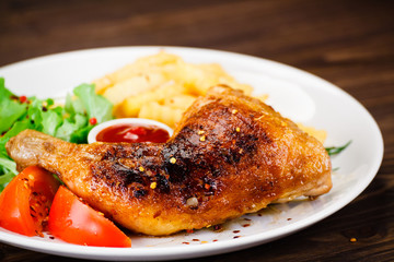 Roasted chicken leg with french fries on wooden background