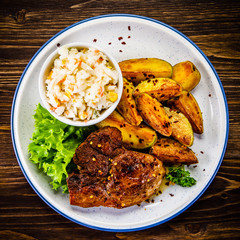 Grilled steak with baked potatoes and vegetables served on wooden table