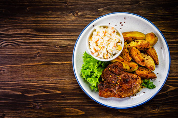 Grilled steak with baked potatoes and vegetables served on wooden table