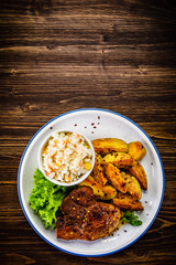 Grilled steak with baked potatoes and vegetables served on wooden table