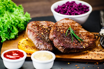 Grilled steak with french fries and vegetables served on black stone on wooden table