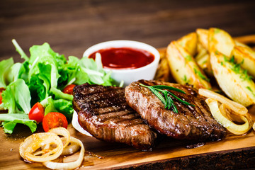 Grilled steak with french fries and vegetables served on black stone on wooden table