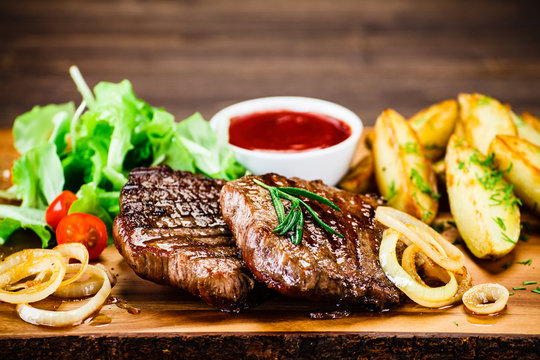 Grilled steak with french fries and vegetables served on black stone on wooden table