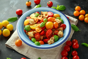 Panzanella Tomato salad with red, yellow, orange cherry tomatoes, capers, basil and ciabatta croutons. summer healthy food.