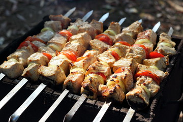 Pieces of juicy slices of marinated pork meat strung on skewers with slices of chopped tomatoes and onion cooking on the grill. Cooking shashlik on the brazier Close-up.