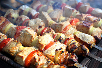 Pieces of juicy slices of marinated pork meat strung on skewers with slices of chopped tomatoes and onion cooking on the grill. Cooking shashlik on the brazier Close-up.