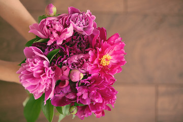  A bright bouquet of home pions is held by women's hands.