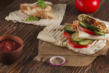 Shaurma, cut in half, meat with vegetables in a bread cake, top view on an old wooden rustic background, on a wooden board with tomato and pepper, copy space