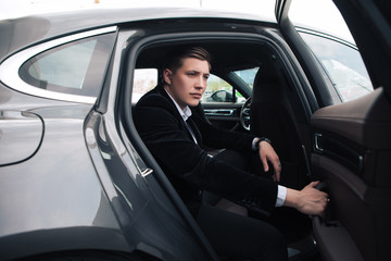 Be smart and intelligent! A handsome serious young businessman sitting into his comfortable new car and going to the office.