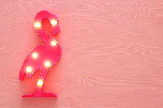 a plastic flamingo lamp with leds over pink wooden background. holiday summer concept.
