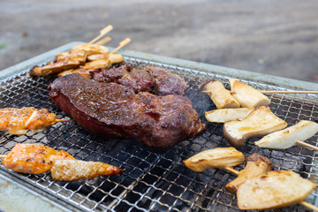 Red raw beef steak is placed on grilled grid over charcoal with fire to make it be cooked well and ready to serve as main dish for family’s dinner.