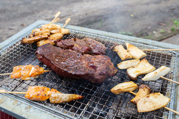 Red raw beef steak is placed on grilled grid over charcoal with fire to make it be cooked well and ready to serve as main dish for family’s dinner.
