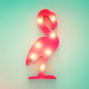 a plastic flamingo lamp with leds over mint wooden background. holiday summer concept.