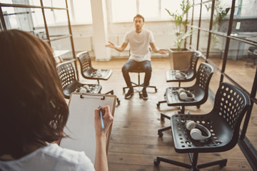 Unhappy man flourishing arms while sitting on chair. Girl writing in clipboard