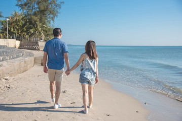 Back side of young couple holding hand and walking on the beach