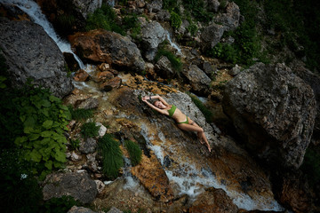 Cute young girl is resting by the waterfall in the mountains