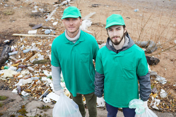Two young men from greenpeace looking at camera on dirty territory during work