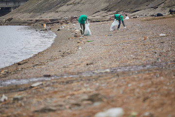 Two greenpeace volunteers picking up litter while walking along coastline in natural environment