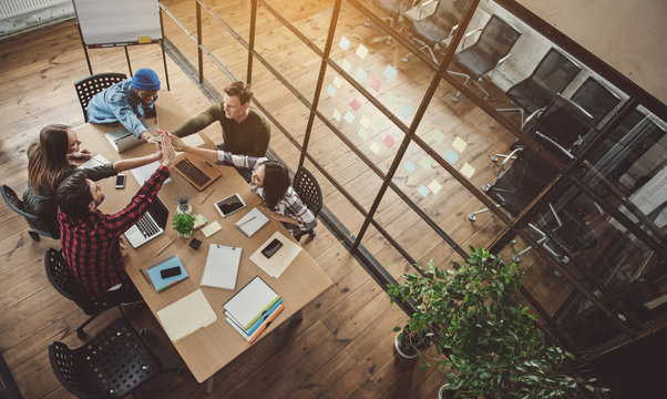 Top view cheerful colleagues taking high five together while locating at desk during job. Glad partners at labor concept