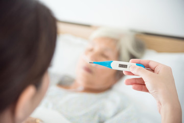 Nurse hand holding thermometer with high temperature result from elderly woman patient