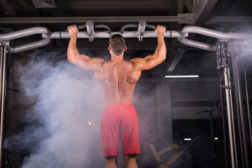 Strong young man doing pull up exercise on horizontal bar in gym