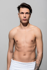 Portrait of pleasant attractive shirtless teenager is standing and demonstrating his perfect and healthy body. He is looking forward thoughtfully with white towel on his hips. Hale and hearty concept