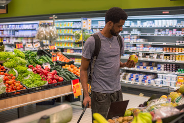 African man with beard standing in supermarket, choosing fruits. Vegetable and milk showcases on background