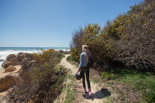 Woman holding helmet for motorcycle travel walking on ocean beach. Algarve, Portugal