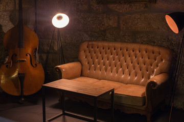Modern jazz bar interior design, leather sofa, cello music instrument, lamps. Stone wall on...