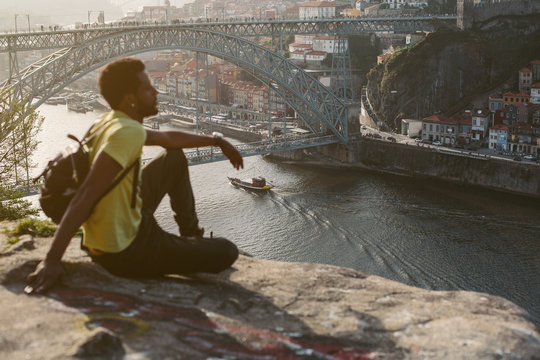 Traveler african man enjoying city view in Porto, famous iron bridge, boat and Douro rive on background