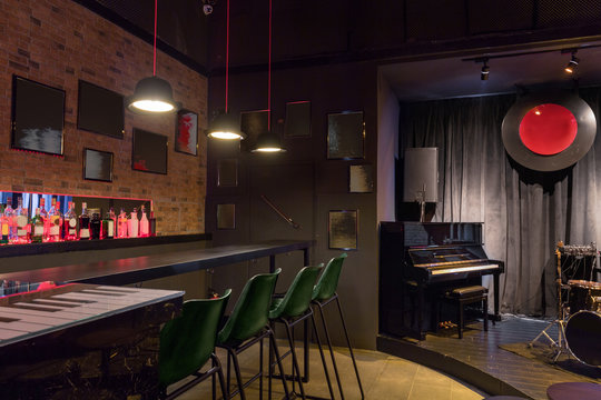 Modern jazz bar interior design, stage with black piano, lamps above bar counter