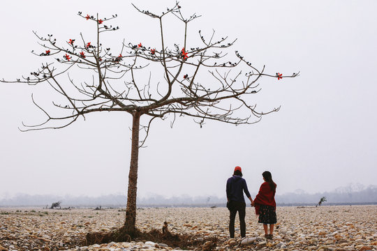 Travel couple standing under tree in fog river beach, fresh morning time. Chitwan national park, Nepal