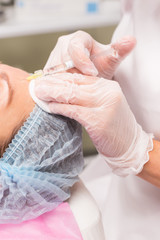 Close up of hands of expert beautician injecting in female forehead