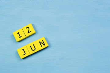 JUN 12, yellow cube calendar on blue wooden surface with copy space